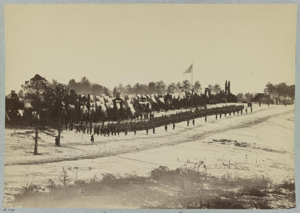 Camp of 2nd Maine Infantry, Camp Jameson-Photograph shows officers, infantry soldiers, and military band standing in a snow covered field; tents in the background.